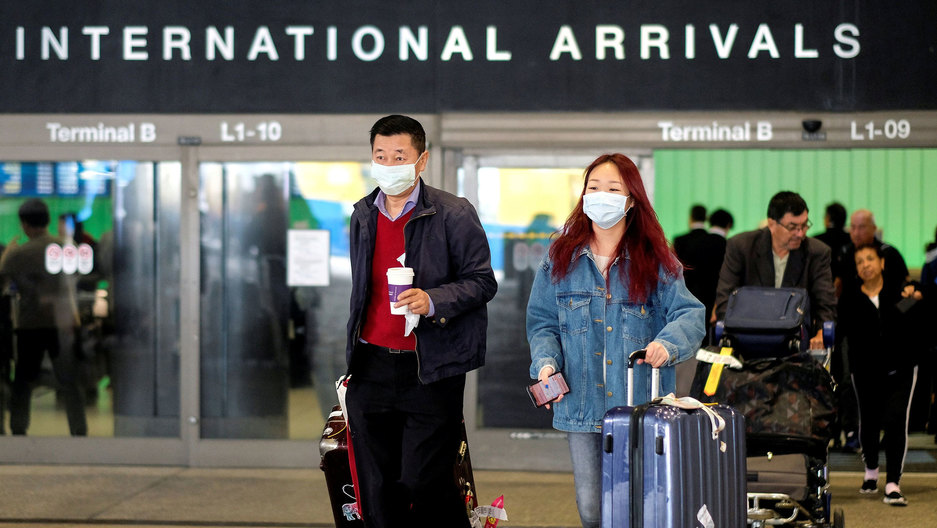 Passengers leave Los Angeles International Airport after arriving from Shanghai, China. A man and a woman are shown with suitcases and wearing face masks while leaving the international arrivals terminal at Los Angeles International Airport.