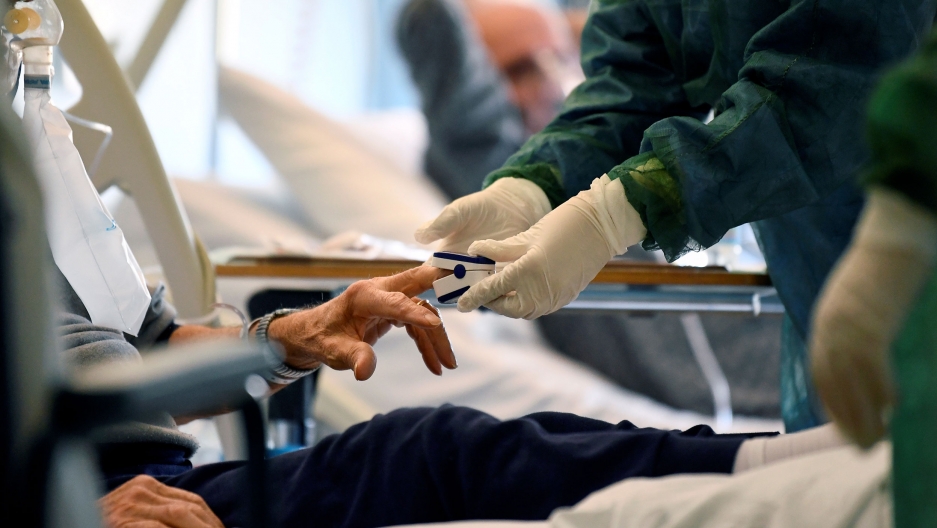 Medical staff in a protective suit treats a patient suffering from coronavirus disease in an intensive care unit at the Oglio Po hospital in Cremona, Italy, March 19, 2020. The hands of a medical professional are shown wearing protective gloves and putting a device on a patient's finger.