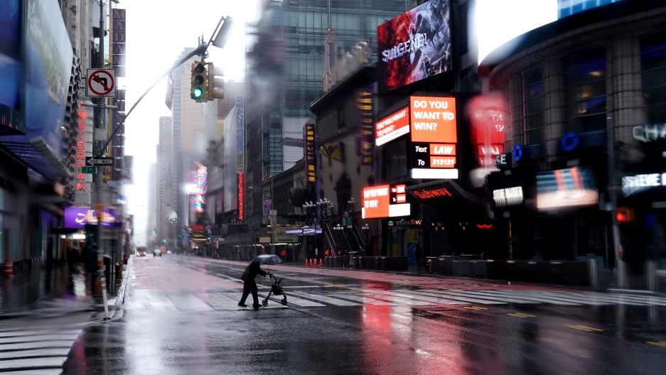 A person with a walker crosses 42nd Street in a mostly deserted Times Square following the outbreak of the coronavirus, in New York City, March 23, 2020. A person with a walker crosses and carrying an umbrella is seen crossing 42nd Street with brightly lit signs all around.