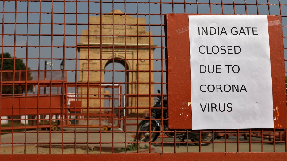 A sign pasted on a security barricade is seen after the India Gate war memorial was closed for visitors amid measures for coronavirus prevention in New Delhi, India, March 19, 2020. A close-up photograph of a reddish metal gate with a motorcycle parked behind it and the India Gate war memorial is shown off in the distance.