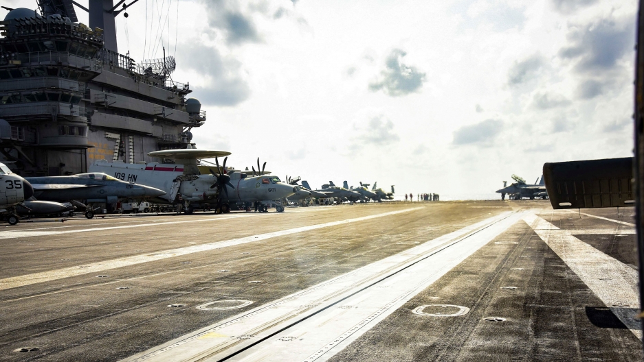 Planes are parked on the flight deck of the US Navy aircraft carrier USS Theodore Roosevelt in the Philippine Sea, March 18, 2020. A photograph taken from the deck of the USS Theodore Roosevelt aircraft carrier with the ship's tower and several airplanes in the background.