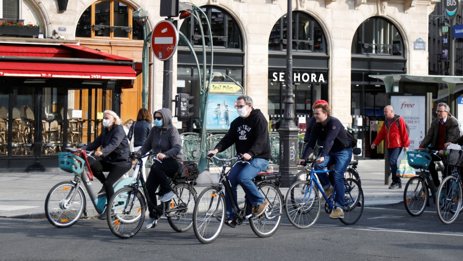 Bikers ride past a metro station after France began a gradual end to a nationwide lockdown due to the coronavirus, in Paris, France, May 13, 2020. A group of several people are shown riding bicycles in the streets and wearing protective face masks.