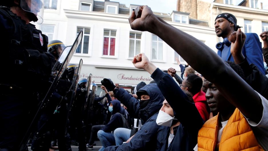 Protesters raise their fists during a demonstration in memory of Adama Traoré, a 24-year-old black Frenchman who died in a 2016 police operation which some have likened to the death of George Floyd in the United States, on the Place de la Republique in Li A large group of demonstrators are shown kneeling with their fists in the air opposite a row of police carrying large shields.