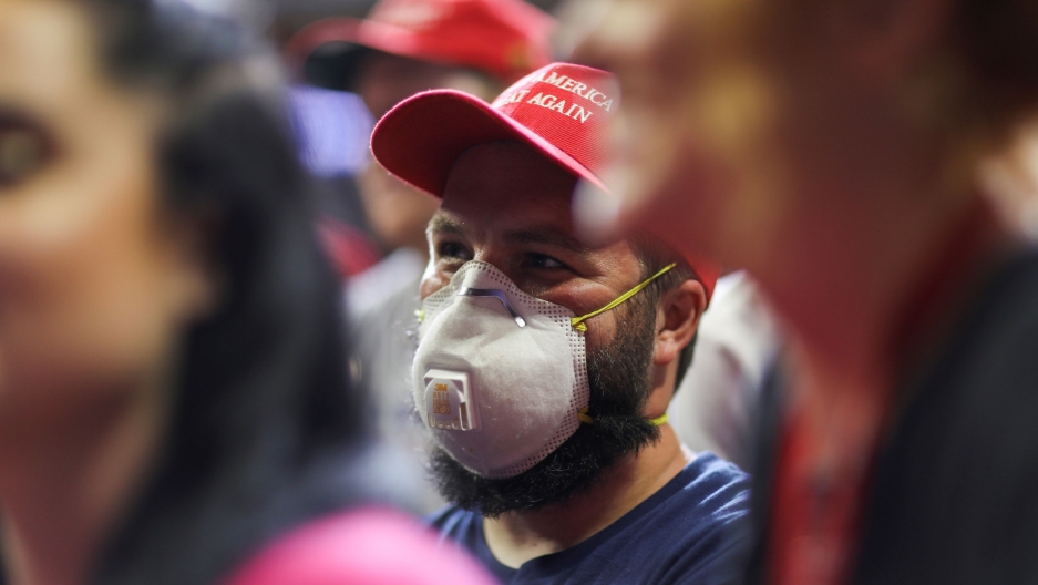 A supporter of US President Donald Trump wears a protective face mask among many other supporters without masks during a campaign rally in Tulsa, Oklahoma, June 20, 2020. A crowd of people are shown with one man wearing a mask and red hat and the people surrounding him without masks.