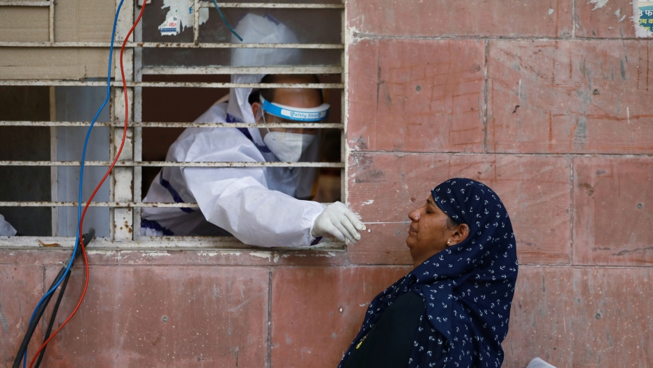 A medical worker collects a sample from a woman at a center to conduct tests for the coronavirus, amidst its spread in New Delhi, India, June 25, 2020. A medical worker is shown reaching through a window with bars on it while wearing protective medical gear and a women outside being tested for the coronavirus.