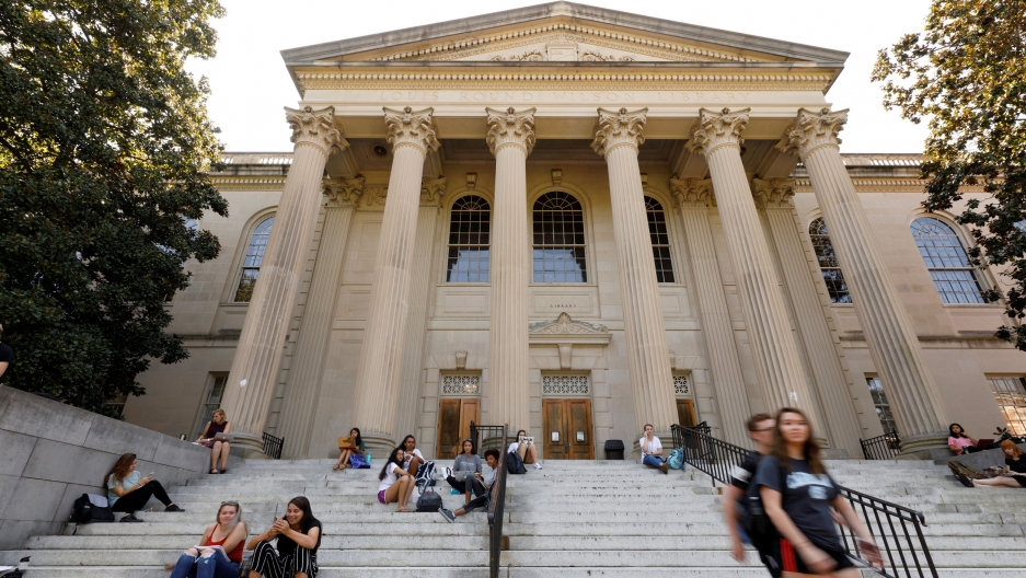 Students sit on the steps of Wilson Library on the campus of University of North Carolina at Chapel Hill, North Carolina. Several students are show sitting on steps with the large Greek columns at the entrance of a college library are shown in the distance.