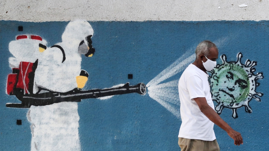 A man walks next to a graffiti depicting a cleaner wearing protective gear spraying viruses with the face of Brazil's President Jair Bolsonaro amid the coronavirus outbreak, Rio de Janeiro, Brazil, June 12, 2020. A painting on a wall shows a person dressed in full head to two medical protective gear with a red backpack and spray hose.