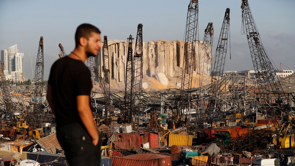 A man looks at the scene of Tuesday's explosion that hit the seaport of Beirut, Lebanon, Friday, Aug. 7, 2020. The port of Beirut is show with shipping containers scattered and damaged in the distance with a man in a dark t-shirt in the nearground.