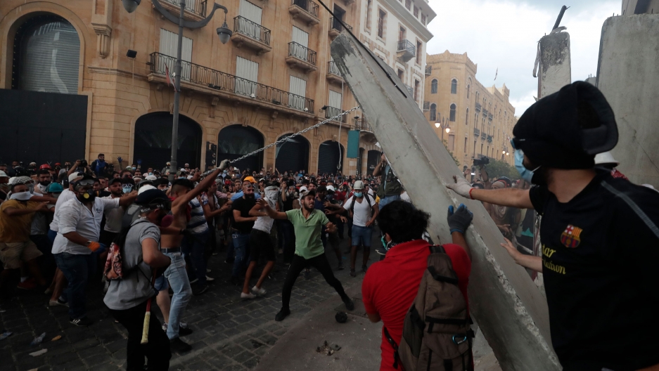 Protesters remove a concrete slab from a barrier to a road leading to the parliament building during anti-government protests following a massive explosion which devastated Beirut, Lebanon, Aug. 10, 2020. A large crowd of protesters are shown in the street with chains pulling down a concrete slab.