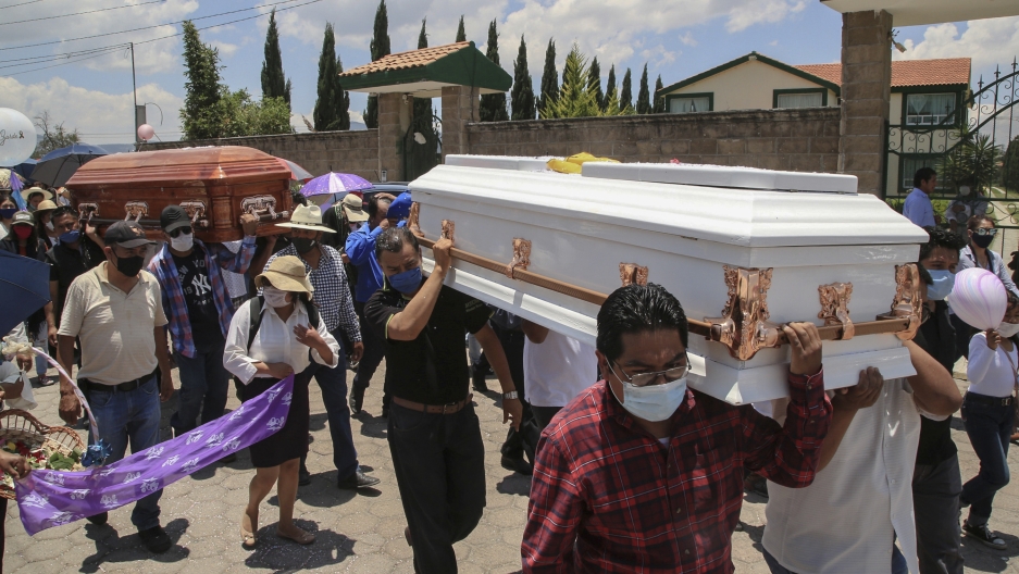 A crowd carries two caskets. 