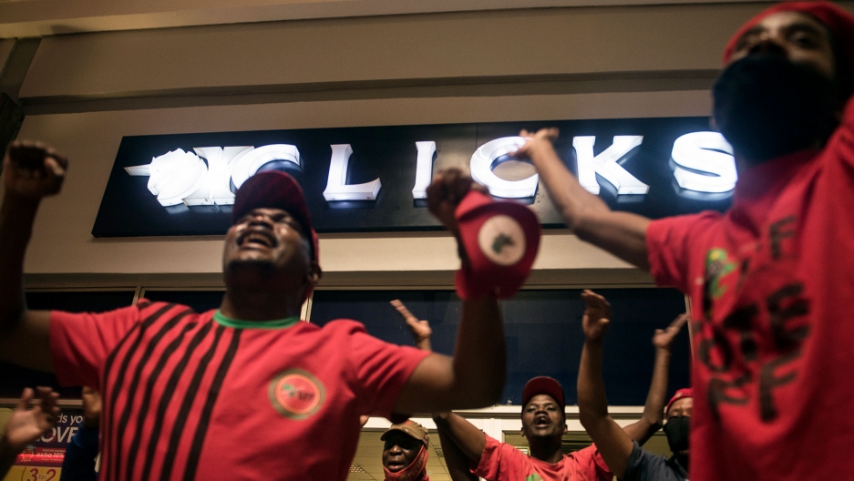 Economic Freedom Fighters (EFF) supporters protest outside a Clicks store in Soweto, Johannesburg, calling for closures after the chain store posted an advertisement on their website that negatively described natural Black hair, Sept. 7, 2020. A group of people are shown protesting outside of a Clicks story with their hands raised.