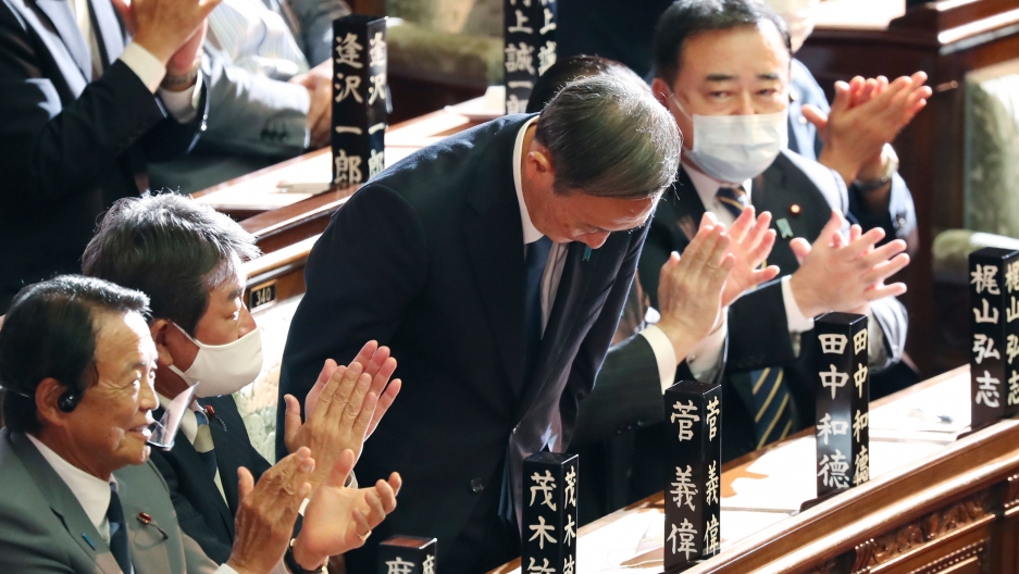 Yoshihide Suga bows after being elected as Japan's new prime minister at the parliament's lower house in Tokyo, Sept. 16, 2020. Yoshihide Suga is shown bowing and surrounded by parliamentarians on either side clapping their hands.