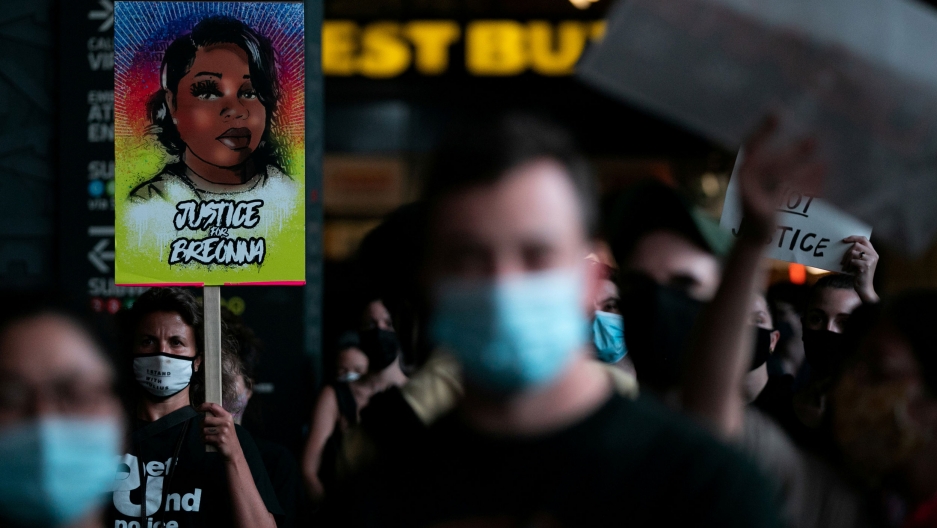 People hold placards during a march following the announcement of a single indictment in the Breonna Taylor case, in New York City, New York, Sept. 23, 2020. A large crowd of people are shown in the dark of night with a woman holding a placard with an illustration of Breonna Taylor on it.