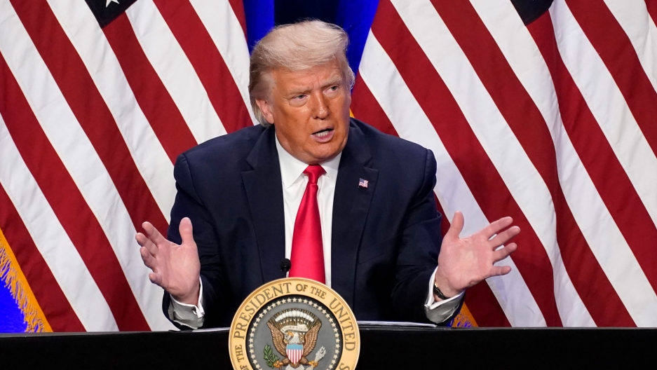 President Donald Trump speaks during an event at Trump National Doral Miami resort, Doral, Fla. Sept. 25, 2020. President Donald Trump with his hands outstreched while wearing a dark suit and red tie with US flags behind him.