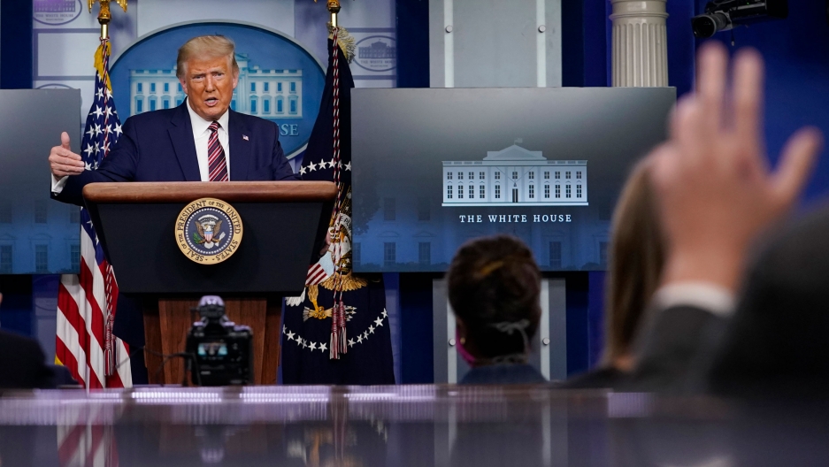 President Donald Trump gestures while speaking during a news conference at the White House, Sept. 27, 2020. President Donald Trump is shown standing at a podium with TV monitoris and US flags behind him.