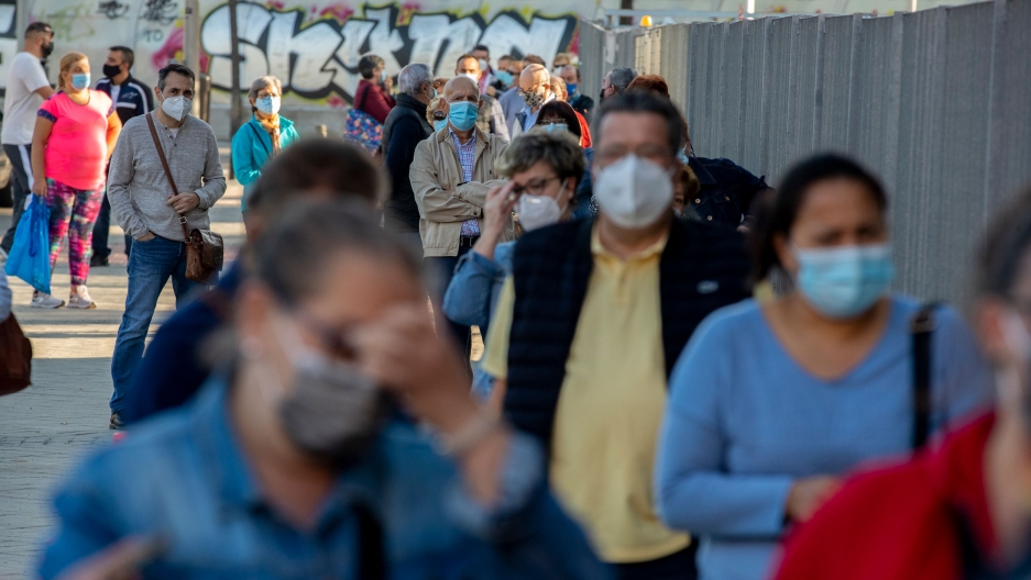 People wait in line for a rapid antigen test for COVID-19 in the southern neighborhood of Vallecas in Madrid, Spain, Oct. 7, 2020. A long line of people are shown wearing face masks with wall painted with graffiti in the distance.