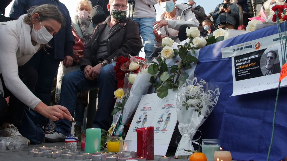 A woman lights a candle on Republique square during a demonstration in support of freedom of speech and to pay tribute to a French history teacher who was beheaded near Paris, Oct. 18, 2020. A large group of people are shown near a make shift memorial with candles and flowers for a teacher who was killed in France.
