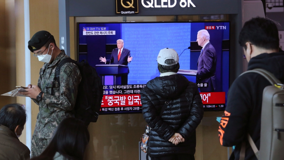 A TV screen shows a live broadcast of US President Donald Trump and Democratic presidential candidate former Vice President Joe Biden during the final presidential debate, at the Seoul Railway Station in Seoul, South Korea, Oct. 23, 2020. Several people are shown standing near and one person watching a TV screen showing the US presidential debate.