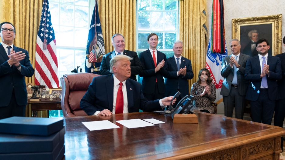 US President Donald Trump hangs up a phone call with the leaders of Sudan and Israel in the Oval Office of the White House, Oct. 23, 2020. Donald Trump is shown sitting at a desk and wearing a dark suit with a red tie and hanging up a phone.