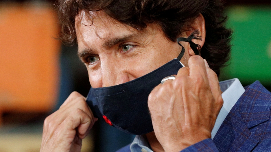 Canada's Prime Minister Justin Trudeau removes his face mask before speaking in Brockville, Ontario, Canada, August 2020. Canada's Prime Minister Justin Trudeau is shown in a close-up photo removing a dark face mask and wearing plaid suit coat.