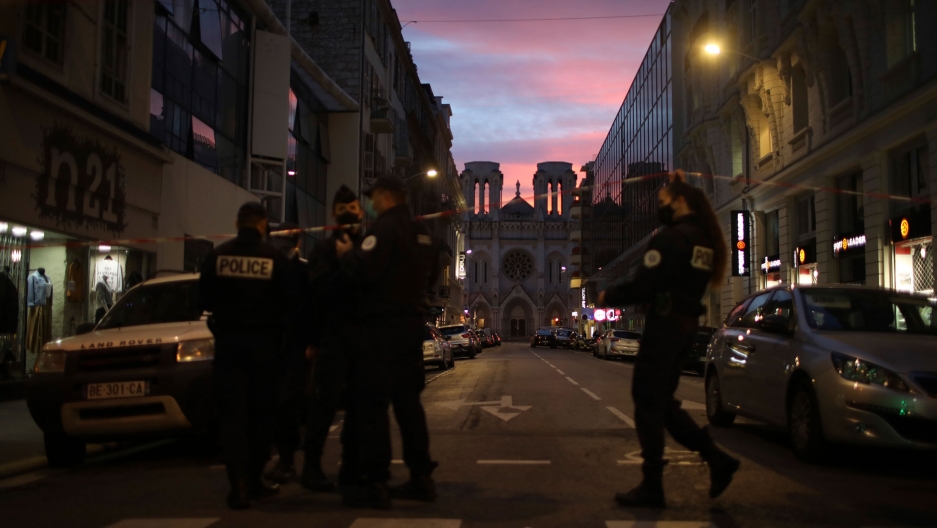 Police work behind a restricted zone near the Notre Dame church in Nice, southern France, after a knife attack took place, Oct. 29, 2020. Several police are shown at the end of a street with the Notre Dame church in the distance and the sun setting.