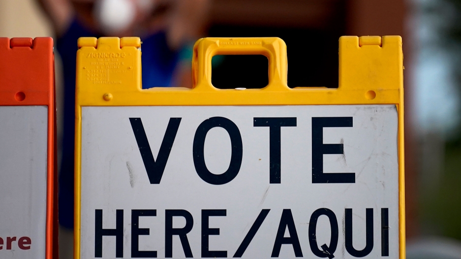 A "Vote Here" sign outside of a polling station, Nov. 3, 2020, in Glendale, Ariz. A plastic yellow sign is shown with "Vote Here/Aqui" printed on it.