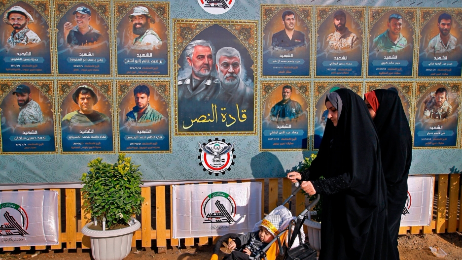 People pass by posters of Gen. Qassem Soleimani, center left, head of Iran's Quds force and fighters killed in fighting during the anniversary procession in the cemetery in Najaf, Iraq, Jan. 4, 2021. People pass by posters of Gen. Qassem Soleimani along with several other illustrated portraits alongside.
