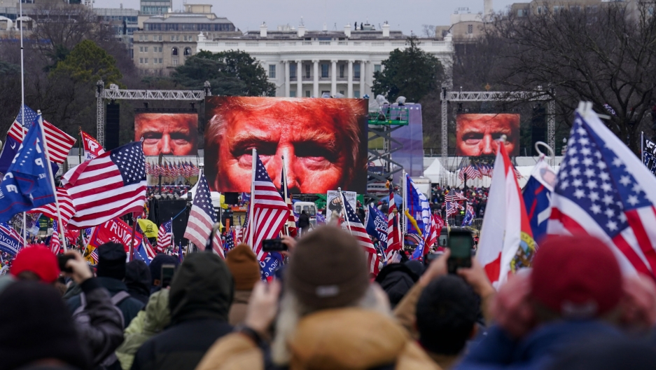 US President Donald Trump supporters participate in a rally in Washington. Far-right social media users for weeks openly hinted in widely shared posts that chaos would erupt at the US Capitol while Congress convened to certify the election results, Jan. 6 A large crowd of people are shown holding small US flags with screens showing Donald Trump's eyes in the distance.