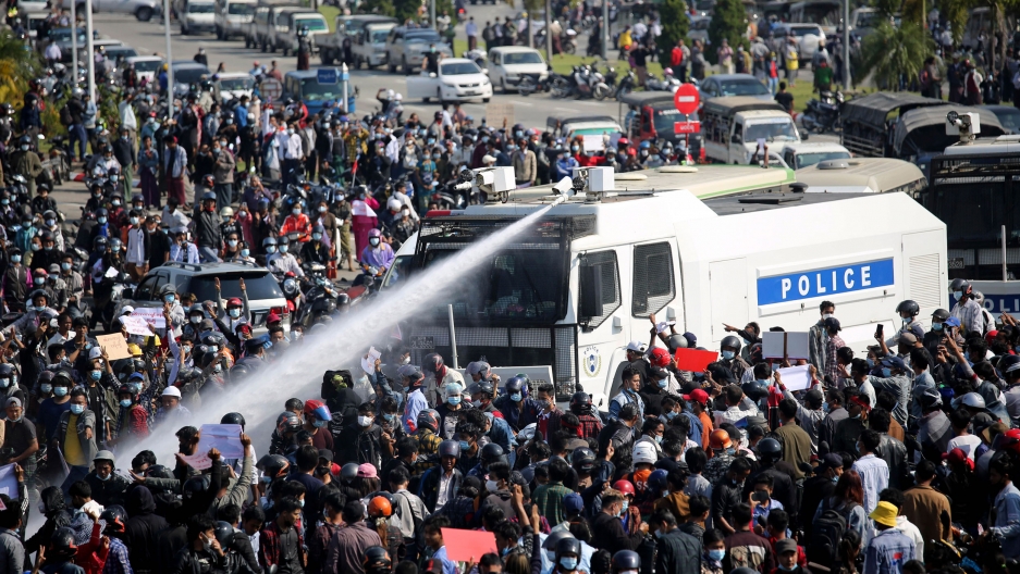 A police truck uses a water cannon to disperse a crowd of protesters in Naypyitaw, Myanmar, Feb. 8, 2021. A large crowd of people are shown surrounding a police truck which is shooting a water cannon into the crowd.