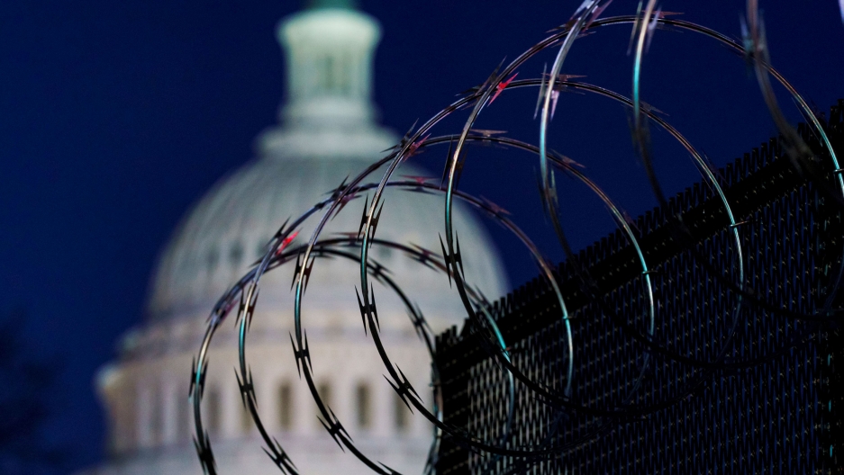 Fencing with razor wire reinforce the security zone on in Washington following a deadly assault on the Capitol, Jan. 19, 2021. A fence with large rings of barbed wire is shown in the nearground with the dome of the US Capitol is soft focus in the background.