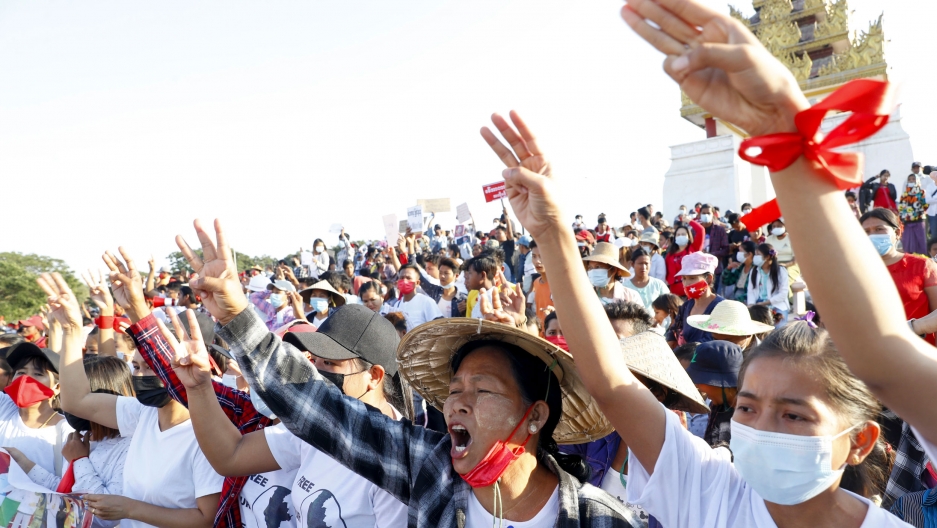 Demonstrators flash three-fingered salutes, a symbol of resistance, against the military coup and shout slogans calling for the release of detained Myanmar leader Aung San Suu Kyi during a protest in Mandalay, Myanmar, Feb. 10, 2021. A large crowd of people are shown, many with their hands raise and holding three fingers in the air with a golden-color shrine seen in the distance.