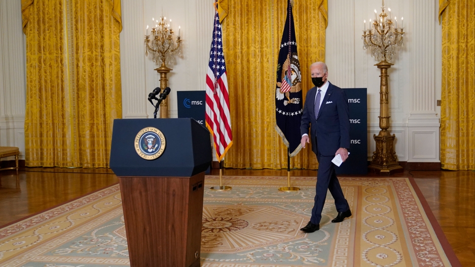 President Joe Biden arrives for a virtual event with the Munich Security Conference in the East Room of the White House, Feb. 19, 2021. President Joe Biden is shown walking toward a podium with the White House crest on it and carrying a white piece of paper.