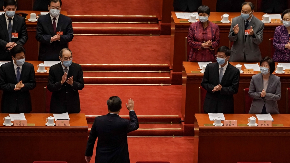Chinese President Xi Jinping waves to delegates upon his arrial for the opening session of National People's Conference at the Great Hall of the People in Beijing, March 4, 2021. Chinese President Xi Jinping is shown with his back toward the camera and facing several rows of government officials who are clapping.