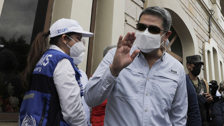 Honduran President Juan Orlando Hernandez waves upon his arrival to an air base to receive a shipment of the AstraZeneca COVID-19 vaccine via the COVAX program, in Tegucigalpa, Honduras, March 13, 2021. Honduran President Juan Orlando Hernandez is shown wearing a medical mask and sunglasses while waving his right hand.