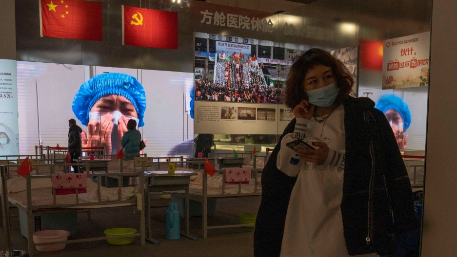 Residents attend an exhibition on the city's fight against the coronavirus in Wuhan in central China's Hubei province on Jan. 23, 2021. A woman is shown holding a mobile phone and wearing a face mask with an image of a medical worker on display in the background.