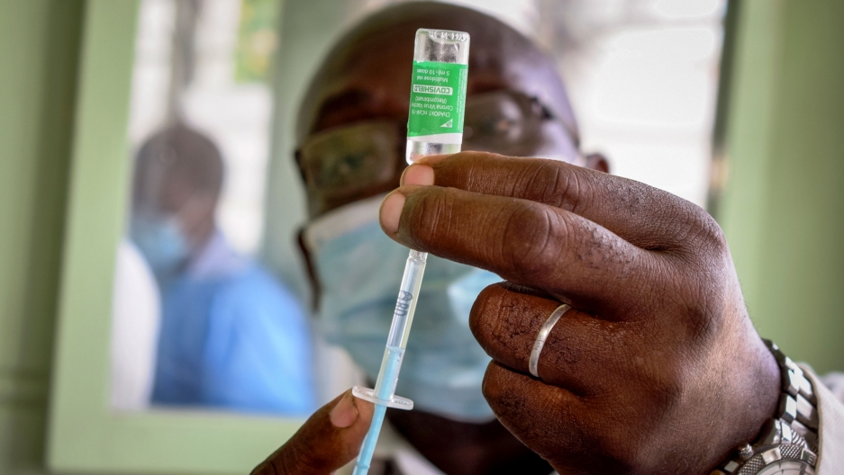 A nurse prepares to administer an AstraZeneca COVID-19 vaccine provided through the global COVAX initiative, to a health worker at the Coast General Teaching & Referral Hospital in Mombasa, Kenya, March 9, 2021. A man is shown with his hand holding a vile and syringe in focus while his face is in the background in soft focus.
