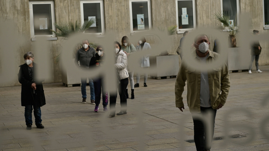 People wait in line for the AstraZeneca COVID-19 vaccine, at San Pedro Hospital, in Logrono, Spain, March 24, 2021. People are shown waiting in a line through a window with frosted lettering.