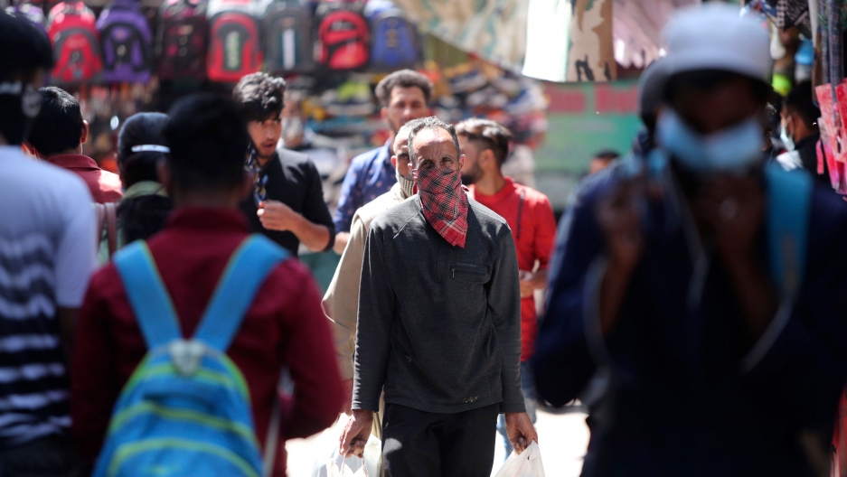 Passengers wearing masks as a precaution against the coronavirus walk for transportation at a bus station in Jammu, India, April 3, 2021. A crowd of people are shown in the street with one man in the center fram wearing a scarf over his face.
