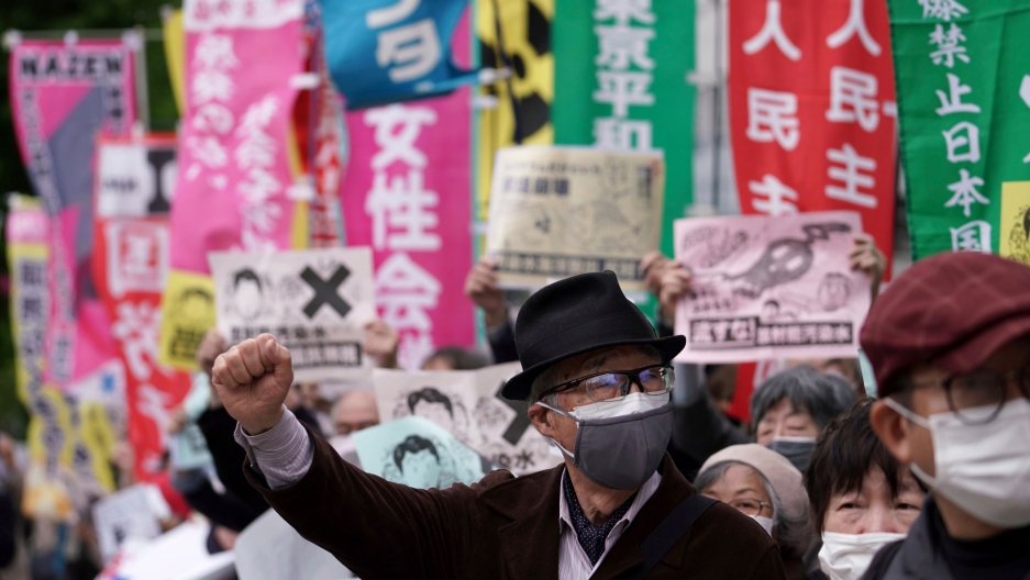 People chant slogans against government's decision to start releasing massive amounts of treated radioactive water from the wrecked Fukushima nuclear plant into the sea, during a rally outside the prime minister's office in Tokyo, Japan, April 13, 2021. A man is shown among a crowd of protesters wearing a dark jacket, hat and face mask with his right hand in the air.