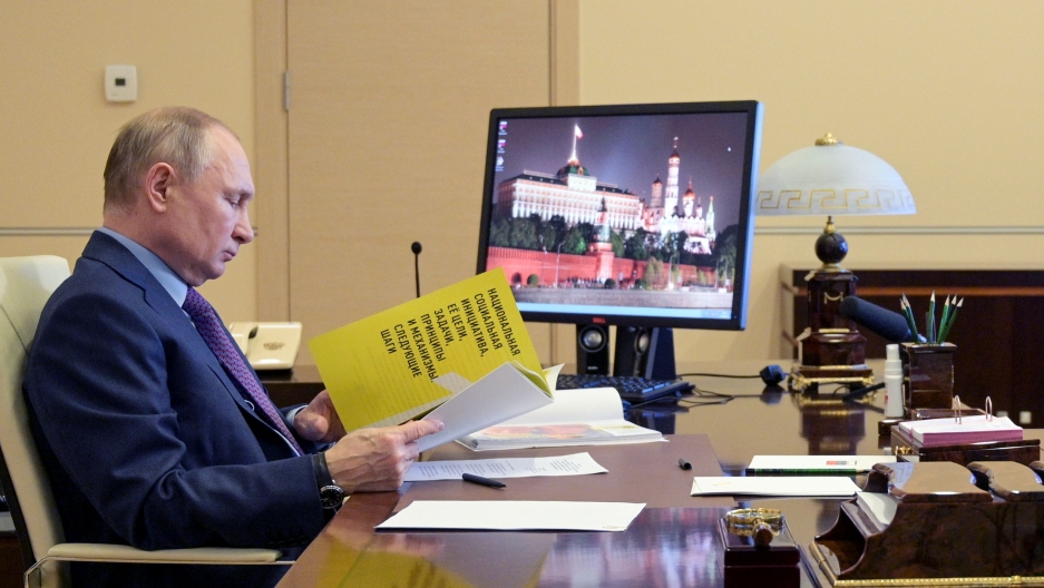 Russian President Vladimir Putin attends a meeting via video conference at the Novo-Ogaryovo residence outside Moscow, Russia, April 15, 2021. Russian President Vladimir Putin is shown sitting at a desk and looking down at a yellow document.
