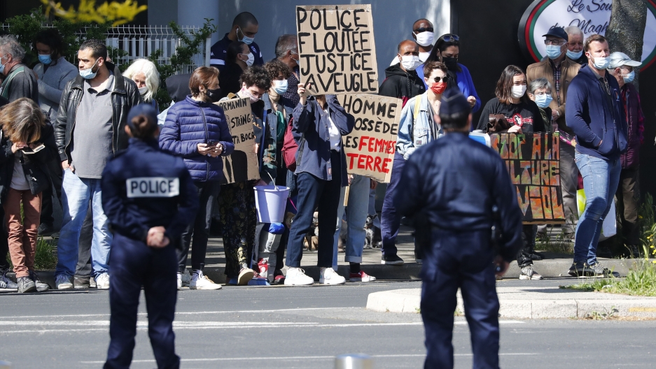 Protesters hold placards reading "Police Blurred, Blind Justice" against the newly voted global security law as French President Emmanuel Macron visits the police headquarters in Montpellier, Southern France, Monday April, 19, 2021. Two uniformed police stand before a crowd of protesters holding banners and signs