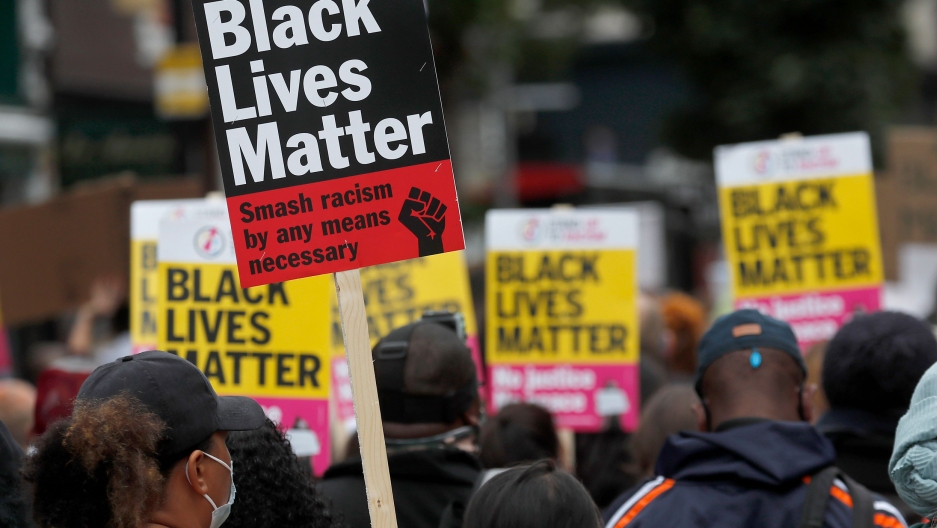 Black Lives Matter protesters hold posters as they march through Notting Hill during the "Million People March" through central London, Aug. 30, 2020. A large crowd of people are show, many holding yellow, red and black placards with Black Lives Matter printed on them.
