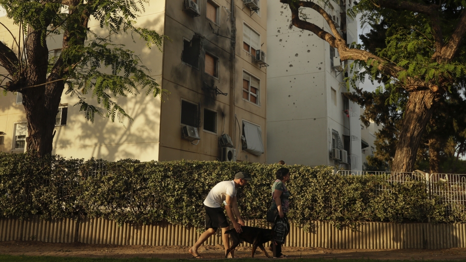 People walk by a damaged residential building after it was hit by a rocket fired from the Gaza Strip last week, in Ashkelon, Israel, Friday, May 21, 2021. People walk by a damaged residential building after it was hit by a rocket fired from the Gaza Strip.