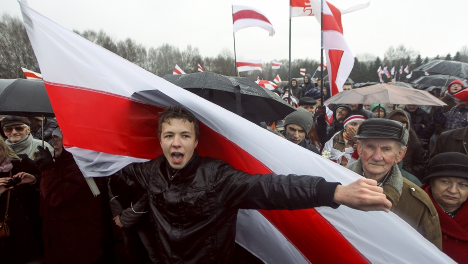 A prominent opponent of Belarus' authoritarian president, Roman Pratasevich, attends an opposition rally in Minsk, Belarus in 2012. Man in black jacket holding red and white flag