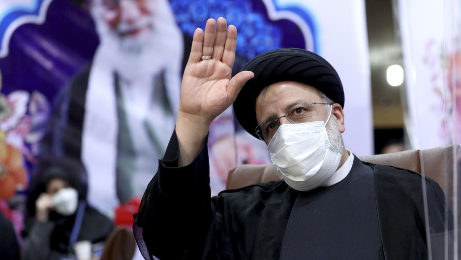 Ebrahim Raisi, head of Iran's judiciary, waves to journalists while registering his candidacy for the upcoming presidential elections Iranian man in black robe and turban waves in front of a picture of Supreme Leader Ali Khamenei
