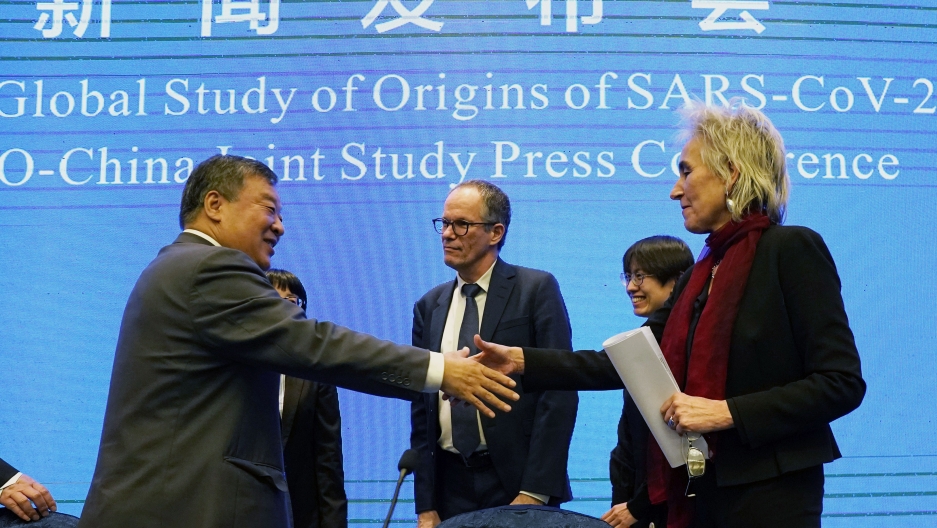 Marion Koopmans and Peter Ben Embarek of the World Health Organization team say farewell to their Chinese counterpart Liang Wannian Marion Koopmans, right, and Peter Ben Embarek, center, of the World Health Organization team say farewell through a handshake with a blue banner in the background