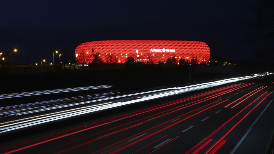 In this Monday, March 16, 2020, file photo, cars pass the illuminated "Allianz Arena" soccer stadium in Munich, Germany. In this Monday, March 16, 2020, file photo, cars pass the illuminated "Allianz Arena" soccer stadium in Munich, Germany.