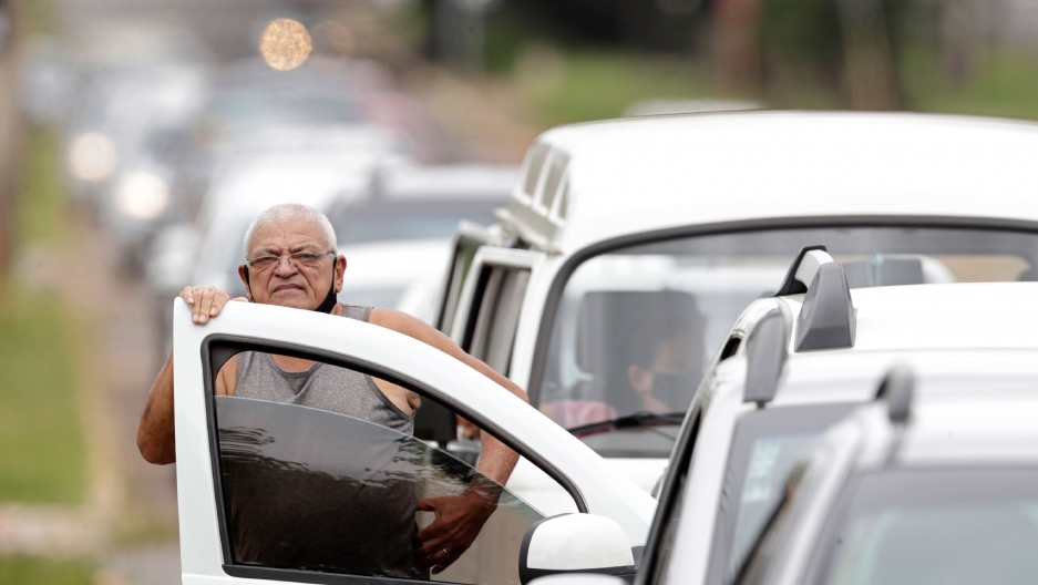 In this March 22, 2021 file photo, a man stands next to his vehicle in a line at a COVID-19 vaccination point for priority elderly persons in the Ceilandia neighborhood, on the outskirts of Brasilia, Brazil. In this March 22, 2021 file photo, a man stands next to his vehicle in a line at a COVID-19 vaccination point for priority elderly persons in the Ceilandia neighborhood, on the outskirts of Brasilia, Brazil.