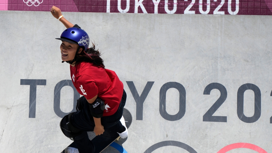 Sakura Yosozumi of Japan competes in the women's park skateboarding finals at the 2020 Summer Olympics, Aug. 4, 2021. Sakura Yosozumi is shown wearing a red shirt and purple helmet while skateboarding down a wall with "Tokyo 2020" painted on it.