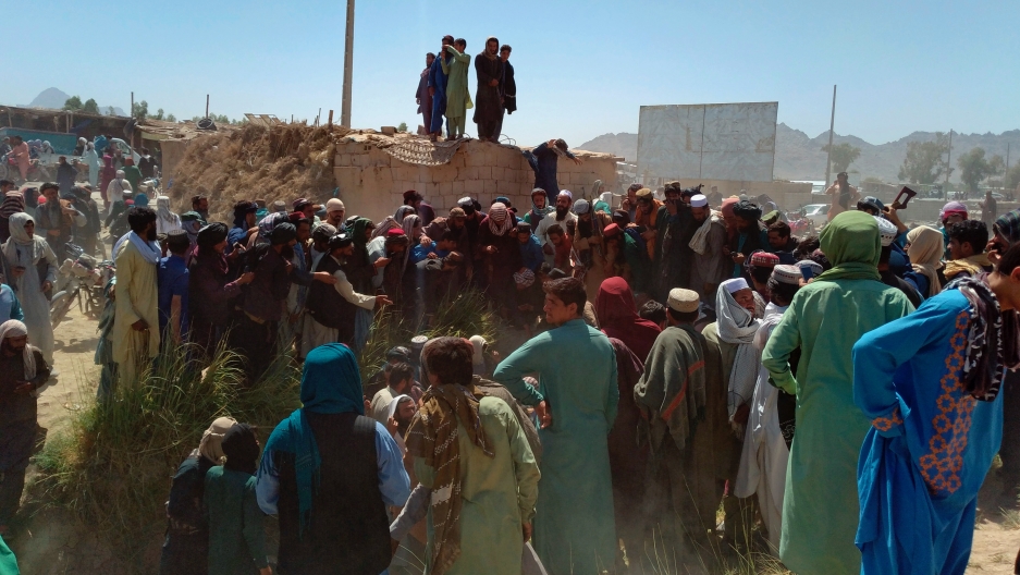 Taliban fighters and Afghans gather around the body of a member of the security forces who was killed Taliban fighters and Afghans gather around the body of a member of the security forces who was killed